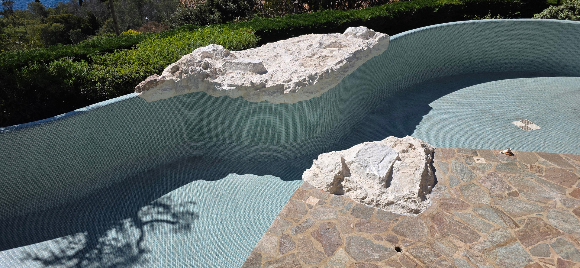 Decorado rocoso a medida para piscina – roca artificial de poliéster en el borde del vaso de mosaico y playa de piedra natural
